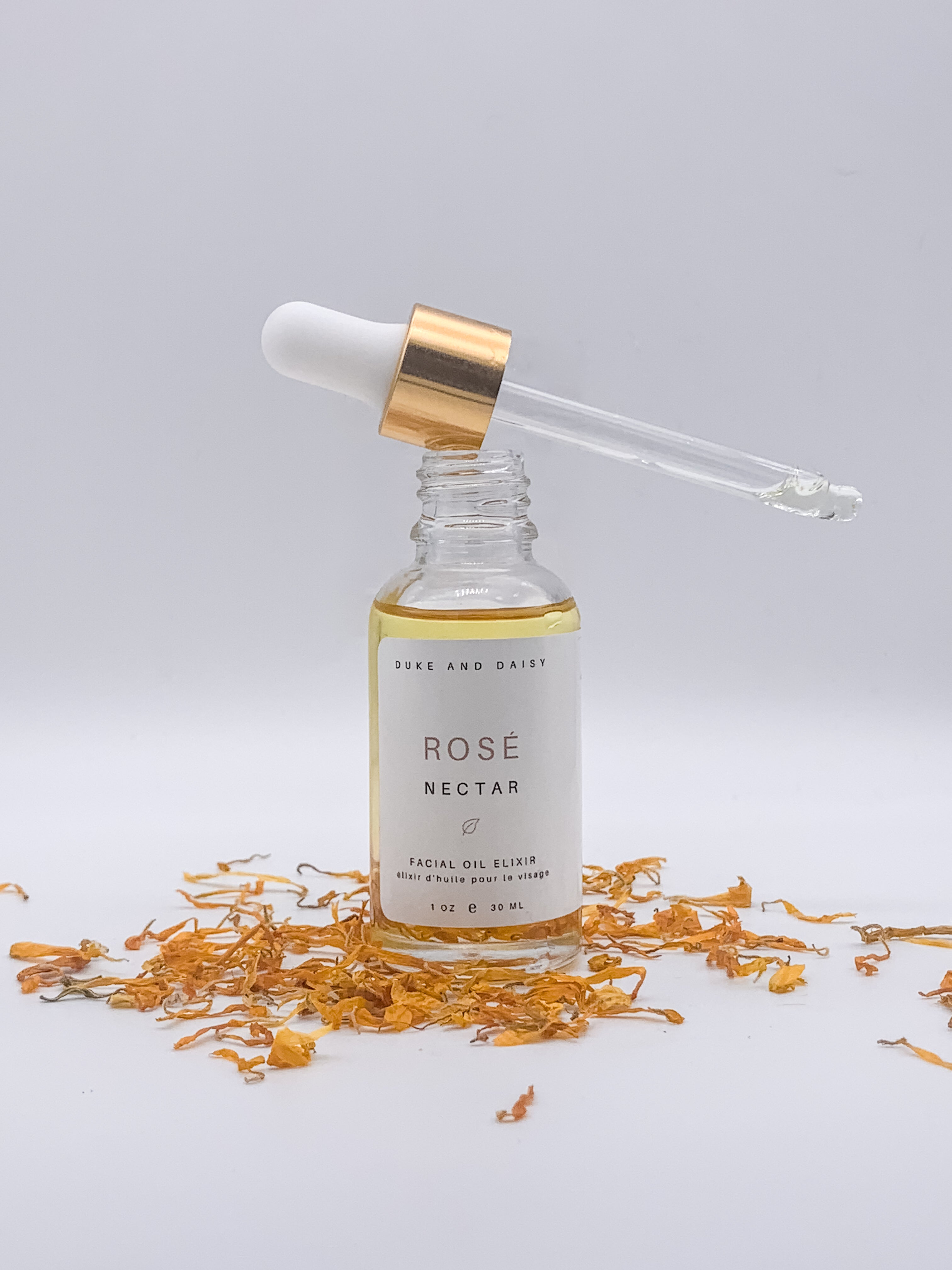 Rose Nectar. The bottle dropper  sits balanced on top of the glass product bottle that is surrounded by calendula leaves. A Facial oil elixir that will transform your skin.